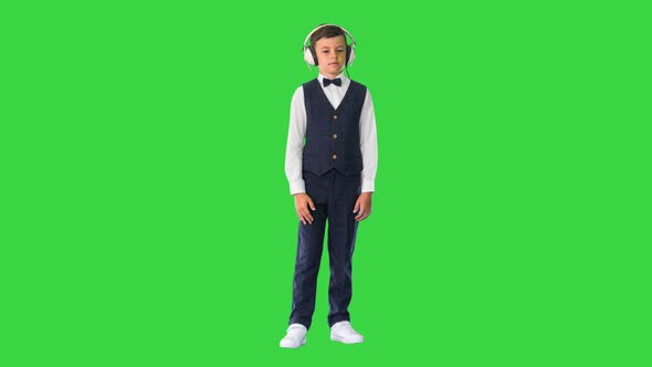Boy in a Bow Tie Listening To Music Keeping Hands on the Headphones on a Green Screen Chroma Key