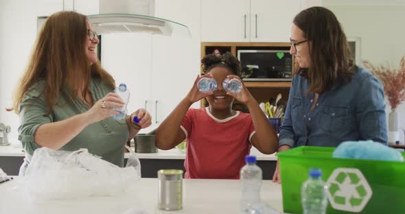 Happy caucasian lesbian couple and their african american daughter sorting waste in kitchen