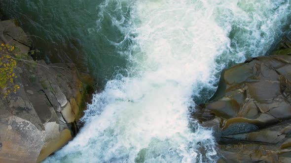 Aerial view of river waterfall with clear turquoise water falling down between wet boulders with alt