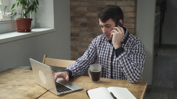 The Man Sitting In The Office Talking On The Phone, Drinking Coffee And Looking At The Computer.