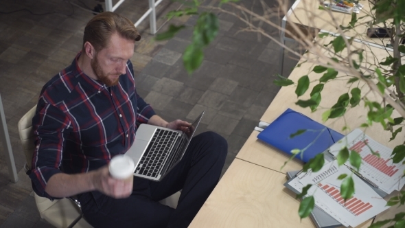 Bearded Man Drinking Coffee And Surf The Internet While Relaxing On a Chair alt