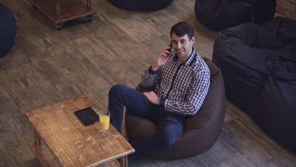 Smiling Man Talking On The Phone, Orange Juice And a Plate On The Table.