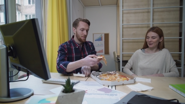 Man And Woman Eating Pizza At Workplace.