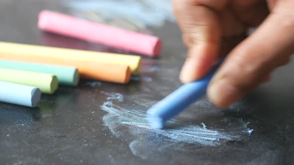 Child Hand Drawing with Colorful Chalk on a Chalkboard on Black Background