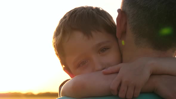 A Happy Little Boy Hugs His Father. The Rays of the Sun at Sunset Illuminate His Face. The Concept