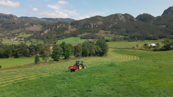 A tractor harvesting grass across farmland and fields in the beautiful nature of Norway