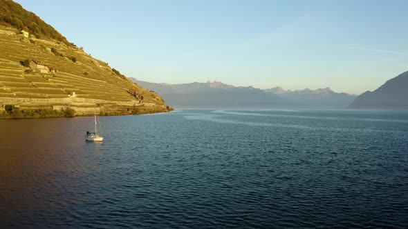 Flying low over Lake Léman in front of Lavaux vineyard, passing next to Sailboat. The Alps in the ba