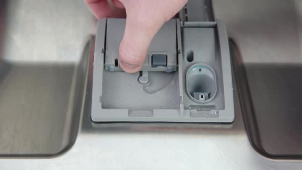 A Man's Hand Puts a Dishwasher Pill in a Closeup Dishwasher in the Kitchen