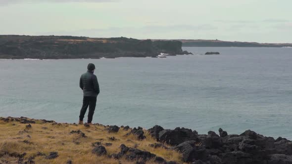 Man stands on cliff looking out at the waves in slow motion