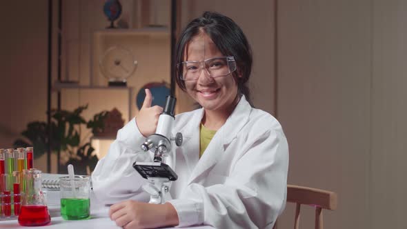 Young Asian Scientist Girl With Dirty Face Looking At Microscope And Showing Thumb Up