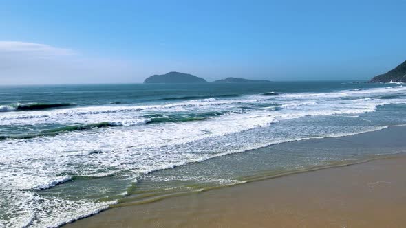 Aerial drone view of ocean waves in open ocean with beach and islands on horizon