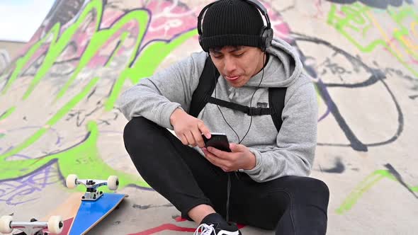 Young Latin Man Skateboarder, with Mobile Phone, Texting at Skate Park