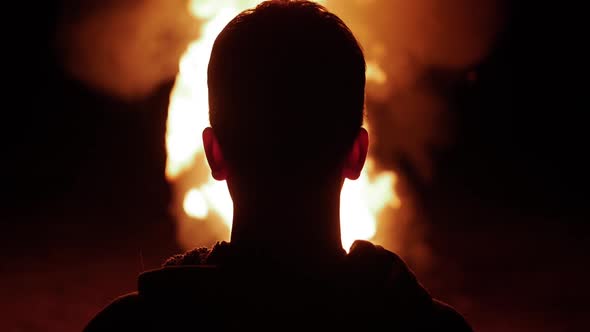 A Teenage Boy Watches A Large Fire Burning In Slow Motion
