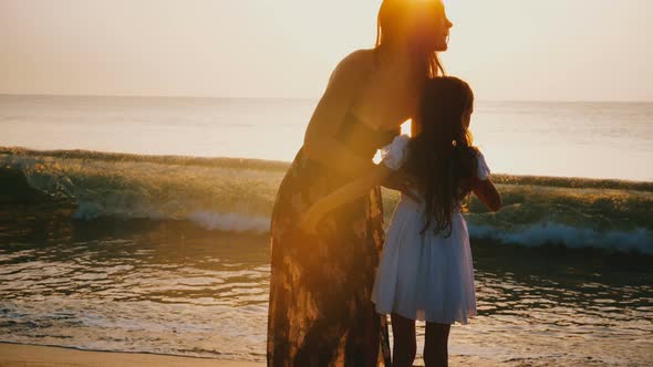 Happy Young Mother Holding and Spinning Little Daughter Smiling at Epic Golden Sunset Beach