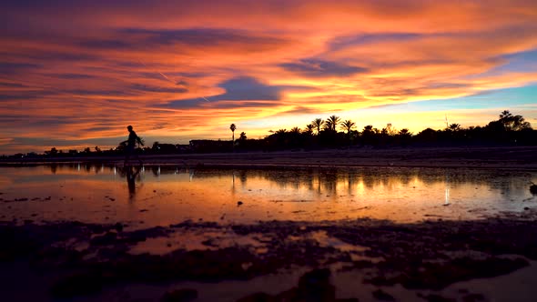 Man tiptoes across a lake in the center of an incredible beach at sunset, the sky and the sun at fal