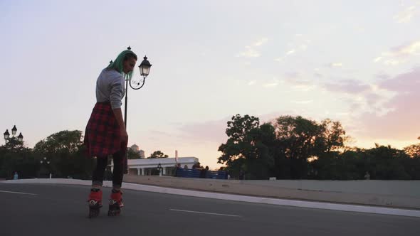 Young Stylish Funky Girl with Green Hair Riding Roller Skates in Park Slow Motion