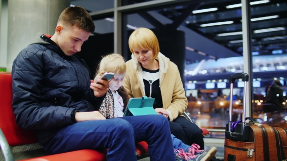 Mom And Two Kids Waiting For a Flight, Children Use Smartphone And Tablet