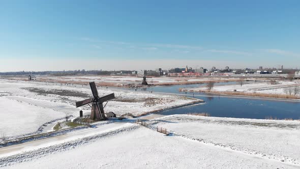 Snowy winter Dutch polders, people ice skating on canal beside windmill, aerial