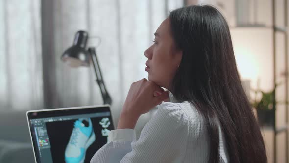 Close Up Of Asian Female Footwear Designer Thinking While Designing Shoe On A Laptop At Home