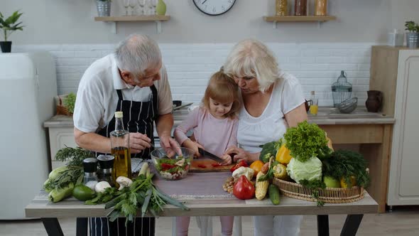 Senior Couple in Kitchen Teaching Granddaughter Child How To Cook, Chopping Pepper with Knife