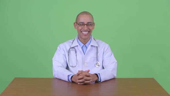 Happy Bald Multi Ethnic Man Doctor Talking Behind Desk