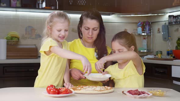 The Children Cook Pizza with Their Mother. The Girls Sprinkle Pizza with Cheese and Help Their
