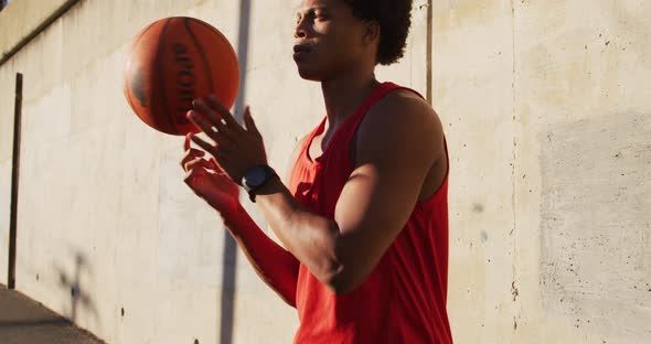 Fit african american man exercising outdoors in city, balancing spinning basketball on fingertip