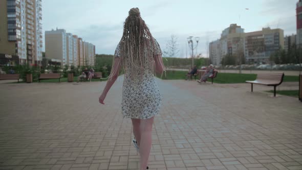 A Cute Young and Happy Girl with Dreadlocks Walks Down the Street and Poses