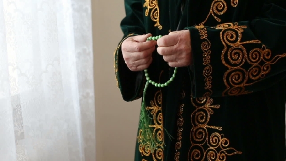 An Old Mullah In National Dress Praying With Rosary Beads In Hands