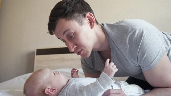 Young Father Entertains Little Baby Girl on Bed at Home