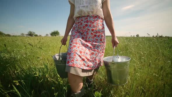 Closeup of a Milkmaid Carrying Buckets and Walking Through Tall Grass