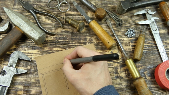 Man Draws a Draft. Indicates Dimensions. Vintage Tools On Background