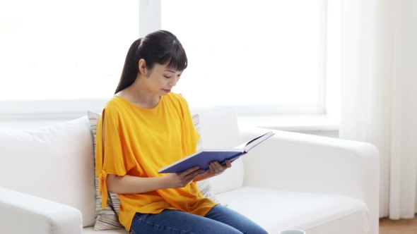 Smiling Young Asian Woman Reading Book At Home