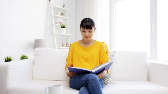 Smiling Young Asian Woman Reading Book At Home