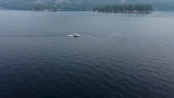 Drone crane shot of a pontoon boat driving from right to left on Payette Lake in McCall, Idaho. This