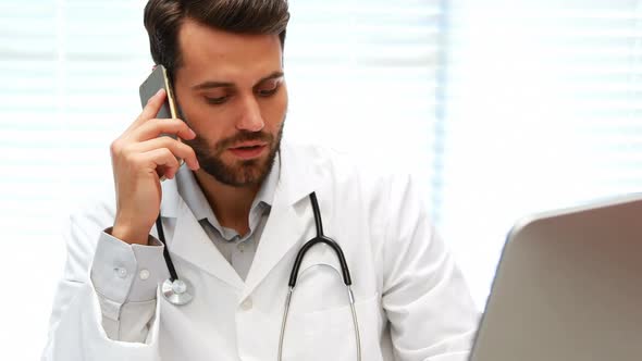 Male doctor talking on mobile phone while working on computer