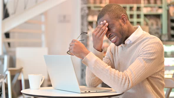 Stressed African Man with Laptop Having Headache in Cafe