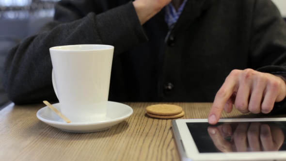 Man in a Cafe Drinking Tea and Working with Tablet