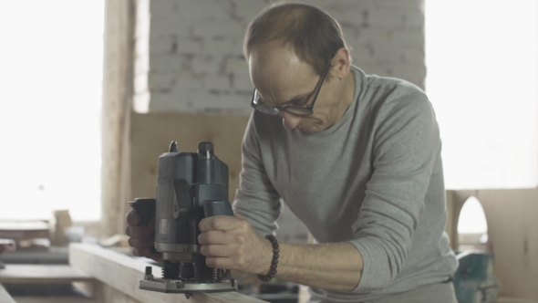 Aged Carpenter Attentively Treat Wooden Board By Plunge Router. Manufacturer