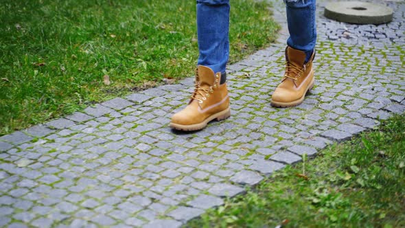 Stylish man's legs outdoors. Male in brown boots walking a stone path. 