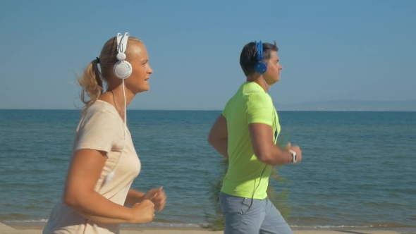 Couple In Headphones Jogging Along The Sea Front alt