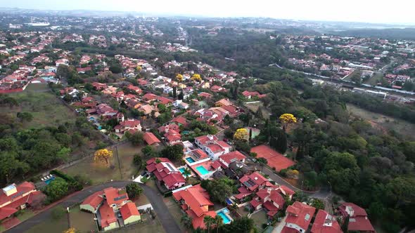 Flyover suburban neighborhood, top view of Houses rooftops between vegetation with yellow tree spots