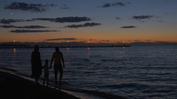 Parents And Child Walking By The Sea In Dusk