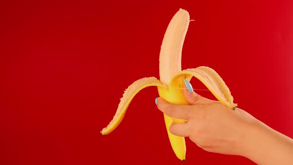 Woman's hand holds semi-peeled banana on red background.