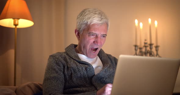 Portrait of Tired Senior Man Working in Home Office on Laptop and Yawning