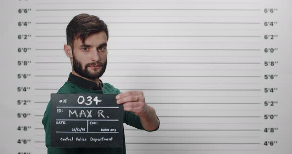 Side Profile Mugshot of Handsome Guy with Beard Holding Sign While Being Photographed in Police