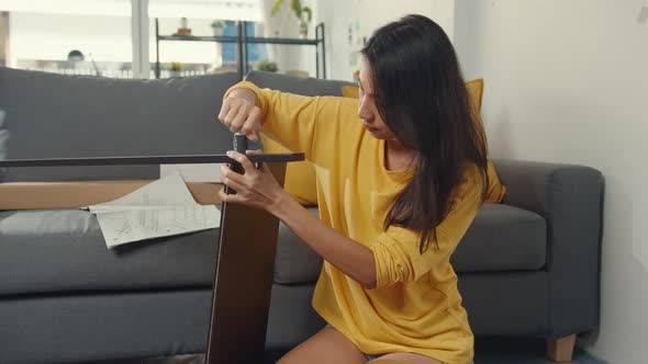 Happy asian young woman unpacking box and reading the instructions to assemble new furniture.