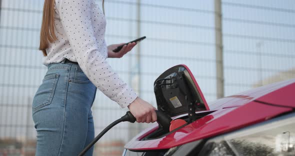 Woman Makes Power Supply Plugged Into an Electric Car Being Charged