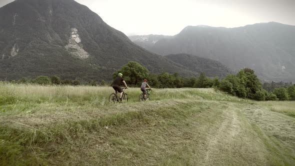 Aerial view of a couple driving mountain bikes on dirt road surrounded by hills.