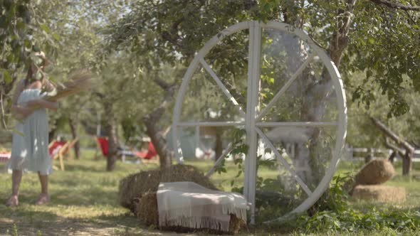 Attractive Young Woman in Straw Hat and Long White Dress in the Green Summer Garden Holding